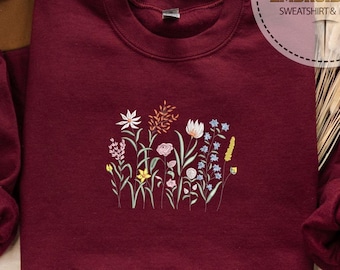 May include: A maroon sweatshirt with a floral embroidery design. The embroidery features a variety of flowers in shades of pink, yellow, blue, and white.