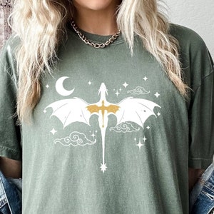 May include: A green oversized t-shirt with a white graphic of a dragon flying in the clouds with a crescent moon and stars.