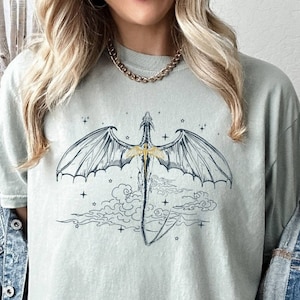 May include: A light green t-shirt with a graphic of a dragon flying in the clouds. The dragon is outlined in black and has gold accents.