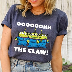 K&ouml;nnte beinhalten: Ein marineblaues T-Shirt mit einem Aufdruck von drei gr&uuml;nen Au&szlig;erirdischen mit dem Text "Ooooooh The Claw!" auf der Vorderseite.