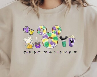 May include: A beige sweatshirt with a purple, green, and yellow Mickey Mouse design and the text "BEST DAY EVER".