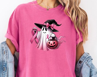 May include: A pink t-shirt featuring a cartoon ghost wearing a witch hat with a pink ribbon and holding a jack-o'-lantern. The ghost has a pink ribbon for breast cancer awareness. The text "Crunchberry" is written in cursive.