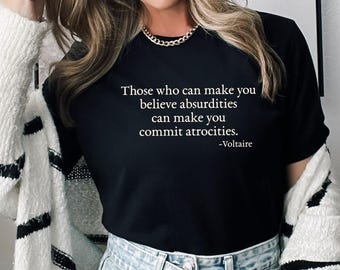 May include: Black crew neck t-shirt with the quote "Those who can make you believe absurdities can make you commit atrocities." by Voltaire in white text. The person is wearing a white and black striped cardigan and light blue denim shorts.