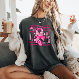 May include: Dark gray t-shirt featuring a pink ribbon design with the word "Fight" in the center. Surrounding the ribbon are words like "Believe," "Love," and "Hope." The shirt is a comfortable, casual style.