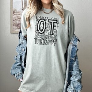 May include: A light green t-shirt with a black graphic design that says "OT Occupational Therapy" with the letters "OT" in a large, bold font.