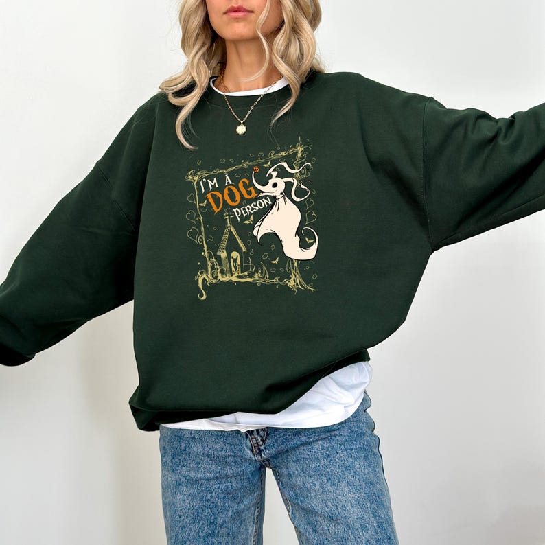 May include: Dark green sweatshirt with the text "I'm a Dog Person" and a cartoon dog graphic. The graphic features a white ghost-like dog with a house and tree design. The sweatshirt is a relaxed fit.