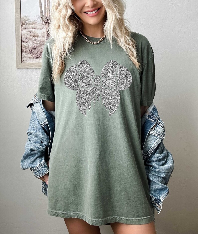 Puede incluir: Una camiseta verde de gran tama&ntilde;o con un dise&ntilde;o de lazo de purpurina plateada.