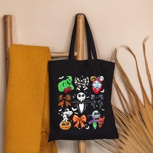 May include: Black tote bag featuring colorful illustrations of characters from The Nightmare Before Christmas. The design includes Jack Skellington, Sally, Oogie Boogie, and other iconic elements. The bag is hanging on a wooden ladder.