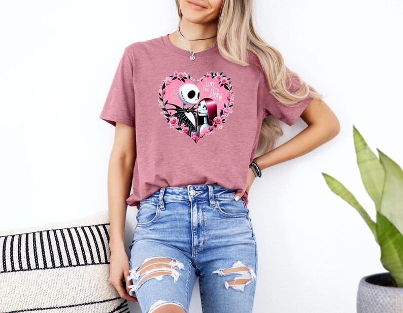 May include: A mauve-colored t-shirt featuring a heart-shaped graphic with Jack Skellington and Sally from The Nightmare Before Christmas. The heart is surrounded by pink roses and the text "Love You Death".