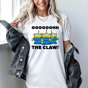 K&ouml;nnte beinhalten: Wei&szlig;es T-Shirt mit einem Aufdruck von drei gr&uuml;nen Au&szlig;erirdischen mit dem Text "OOOOHHH THE CLAW!"