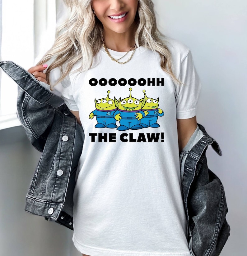 K&ouml;nnte beinhalten: Wei&szlig;es T-Shirt mit einem Aufdruck von drei gr&uuml;nen Au&szlig;erirdischen mit dem Text "OOOOHHH THE CLAW!"