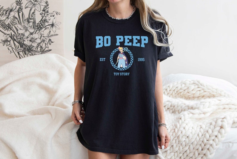 Puede incluir: Camiseta negra con un gr&aacute;fico azul de Bo Peep de Toy Story. El gr&aacute;fico incluye el texto "Bo Peep", "Est. 1995", y "Toy Story".