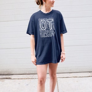 May include: A navy blue t-shirt with a white graphic design that says "OT" with the letters made up of various occupational therapy tools and the words "Occupational Therapy" below.