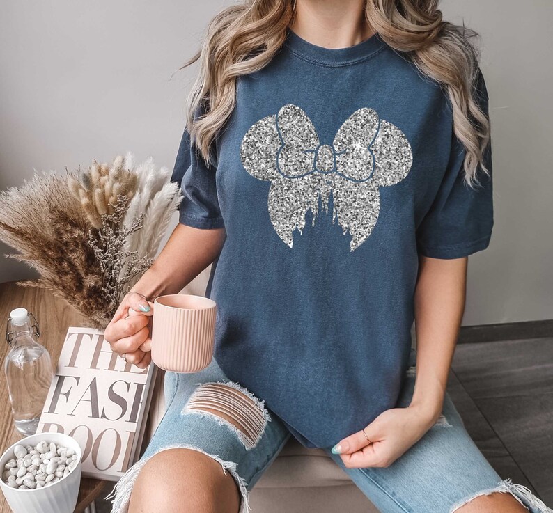 Puede incluir: Una camiseta azul marino con un lazo de purpurina plateado y un dise&ntilde;o de castillo. La camiseta es de gran tama&ntilde;o y tiene mangas cortas.