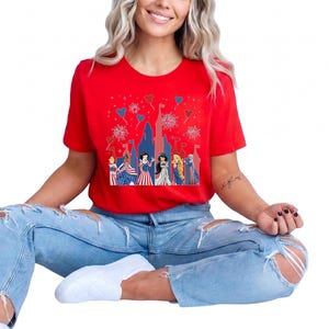K&ouml;nnte beinhalten: Ein rotes T-Shirt mit einem Schlossdesign, Feuerwerk und Zeichentrickfiguren in patriotischer Kleidung. Das Shirt wird mit hellblauen zerrissenen Jeans und wei&szlig;en Schuhen kombiniert. Das Design hat ein festliches Thema.