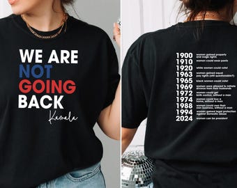 May include: Black t-shirt with the text "WE ARE NOT GOING BACK" in red, white, and blue lettering. The text "Kamala" is written in cursive below the main text. The back of the shirt has a list of dates and women's rights milestones from 1900 to 2024.
