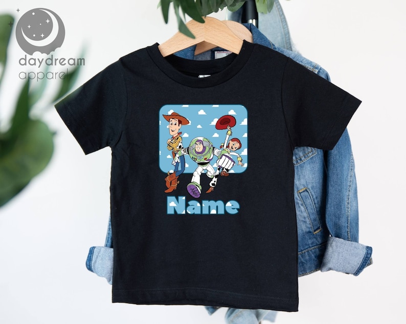 May include: Black short-sleeved t-shirt with a graphic of the Toy Story characters Woody, Buzz Lightyear, and Jessie. The text "Name" is printed below the graphic.