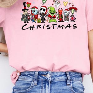 May include: Pink t-shirt with a graphic of cartoon characters from The Nightmare Before Christmas and the text "CHRISTMAS".