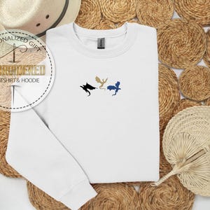 May include: White embroidered sweatshirt with three dragon silhouettes in black, gold, and blue. The sweatshirt is a crew neck style. The text "PERSONALIZED GIFT EMBROIDERED SWEATSHIRT & HOODIE" is in a circular design.