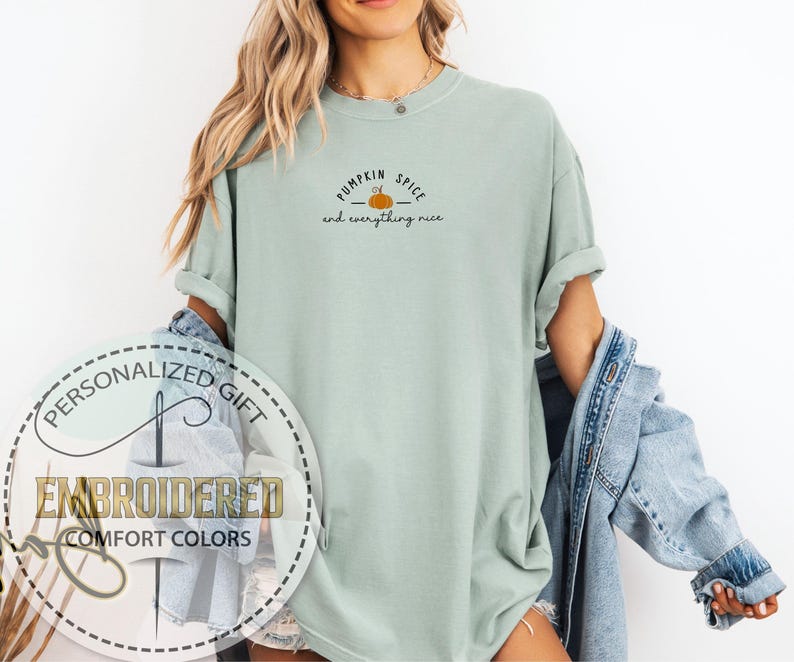May include: A light green t-shirt with the text "Pumpkin Spice and everything nice" and a small pumpkin graphic. The shirt is part of the "Embroidered Comfort Colors" collection and is a personalized gift.