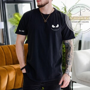 K&ouml;nnte beinhalten: Schwarzes T-Shirt mit einem Jack Skellington-Gesicht. Das Shirt hat den Text "Her Jack" auf dem &Auml;rmel und eine runde Grafik mit der Aufschrift "Personalized Gift" und "Embroidered Comfort Colors".