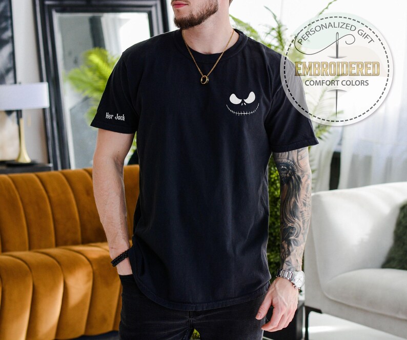 K&ouml;nnte beinhalten: Schwarzes T-Shirt mit einem Jack Skellington-Gesicht. Das Shirt hat den Text "Her Jack" auf dem &Auml;rmel und eine runde Grafik mit der Aufschrift "Personalized Gift" und "Embroidered Comfort Colors".