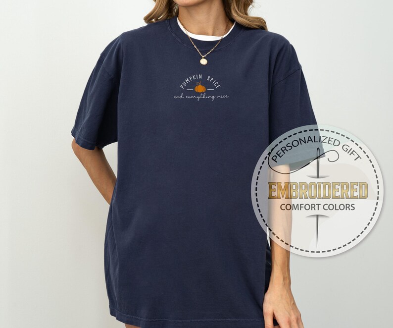 May include: Navy blue t-shirt with the embroidered text "Pumpkin Spice and everything nice" and a small pumpkin graphic. The shirt is a Comfort Colors brand and is a personalized gift.