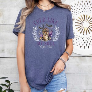 May include: A heather blue t-shirt with a graphic of a coffee cup with bats and the text "Cold Like My Soul Coffee Club".