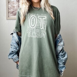 May include: A green t-shirt with a white graphic design that says "OT Occupational Therapy". The graphic design is made up of the letters "OT" surrounded by smaller versions of the letters "OT" and other symbols.