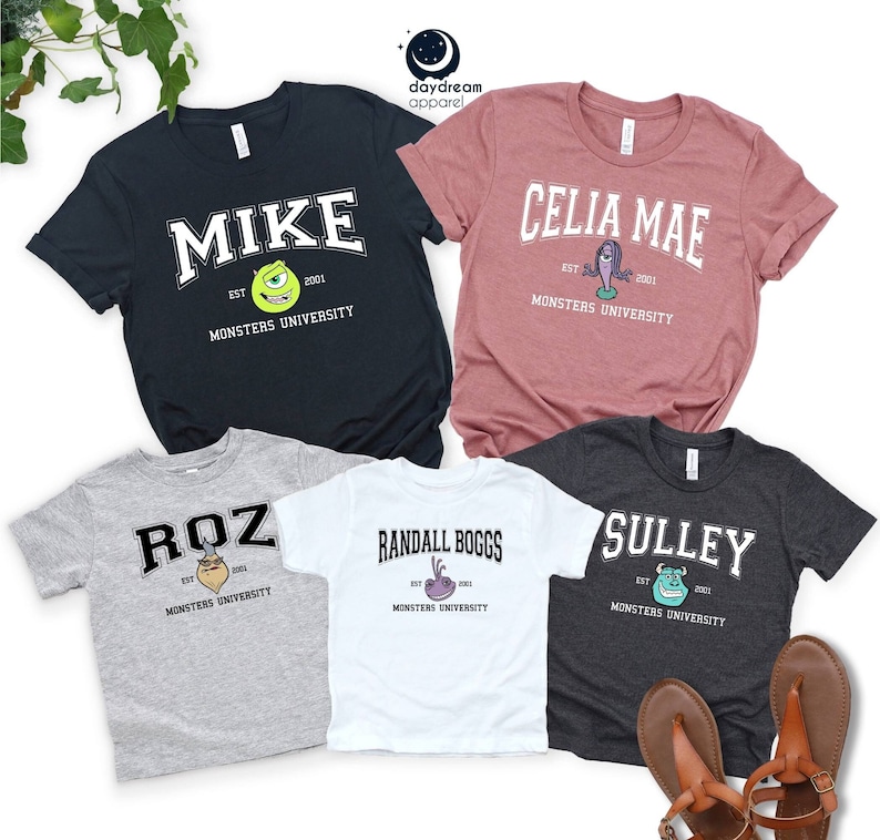 Puede incluir: Cinco camisetas con diferentes nombres de personajes de Monsters University. Las camisetas son azul marino, malva, gris, blanca y carb&oacute;n. Cada camiseta tiene el nombre de un personaje en una fuente universitaria, con una ilustraci&oacute;n de personaje de dibujos animados.
