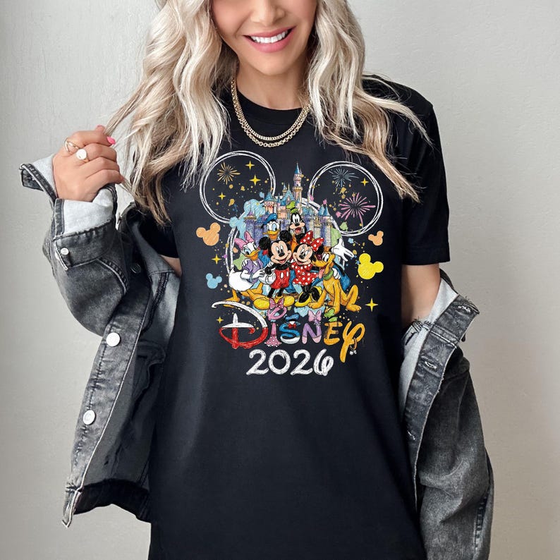 May include: Black t-shirt featuring a colorful Disney design with Mickey and Minnie Mouse, Donald Duck, and other characters. The shirt includes the text "Disney 2026" in a playful font, with fireworks and a castle graphic.