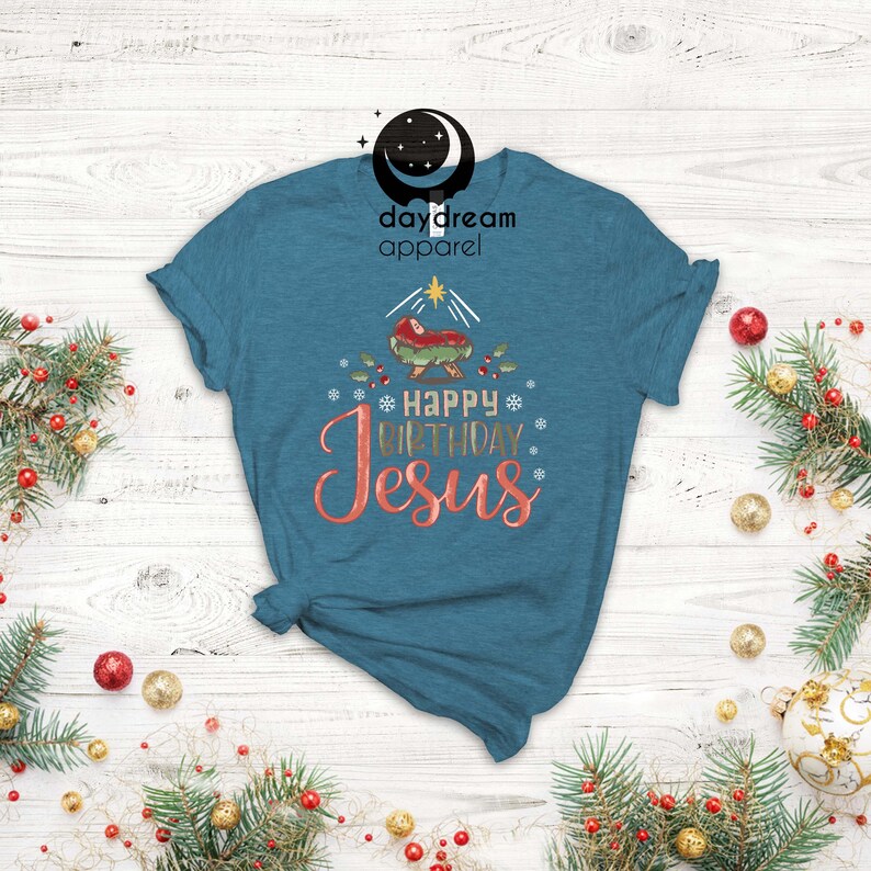May include: A teal blue t-shirt with a Christmas nativity scene and the text "Happy Birthday Jesus" in gold and pink lettering.