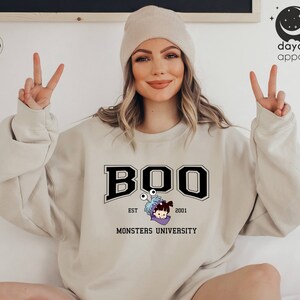 Puede incluir: Sudadera de color arena con la palabra "BOO" en una fuente universitaria negra, con un personaje de dibujos animados de Monsters University. La sudadera tambi&eacute;n incluye el texto "EST 2001" y "MONSTERS UNIVERSITY".