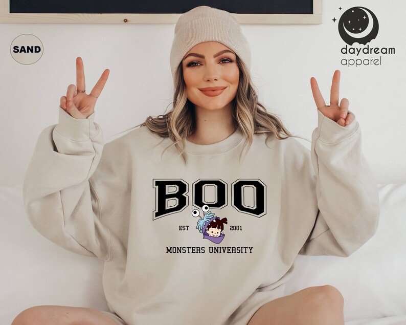 Puede incluir: Sudadera de color arena con la palabra "BOO" en una fuente universitaria negra, con un personaje de dibujos animados de Monsters University. La sudadera tambi&eacute;n incluye el texto "EST 2001" y "MONSTERS UNIVERSITY".