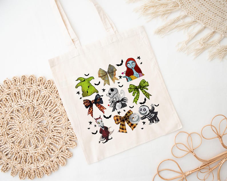 Puede incluir: Un bolso tote de color crema con ilustraciones coloridas de personajes y lazos de una popular pel&iacute;cula animada. El dise&ntilde;o incluye im&aacute;genes de Sally, Jack Skellington y Oogie Boogie, junto con murci&eacute;lagos y estrellas. El bolso tiene dos asas.