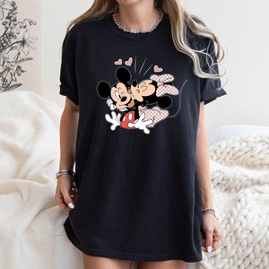 May include: Black t-shirt featuring a graphic of Mickey Mouse and Minnie Mouse kissing. The graphic is in black, red and pink.