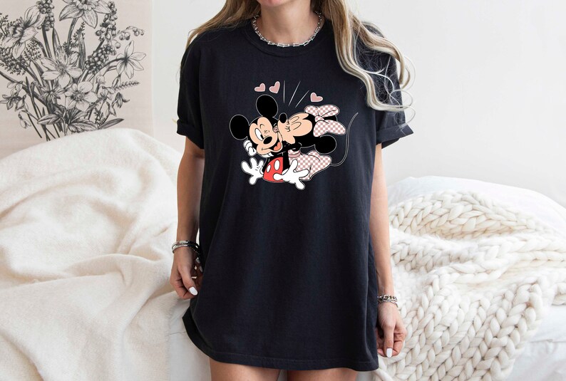 May include: Black t-shirt featuring a graphic of Mickey Mouse and Minnie Mouse kissing. The graphic is in black, red and pink.