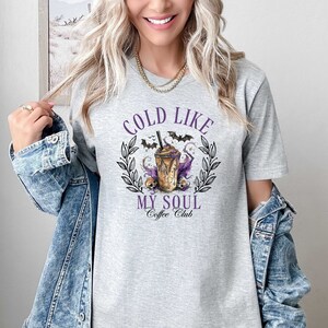 May include: Gray t-shirt with a graphic of a coffee drink with bats and skulls. The text reads "Cold Like My Soul Coffee Club".