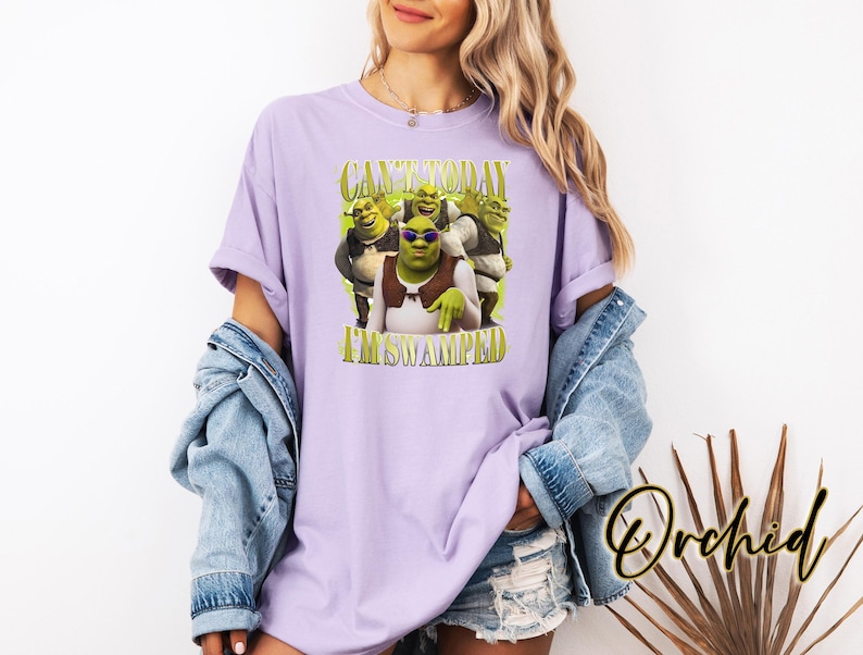 May include: A lilac t-shirt with a Shrek graphic and the text "CAN'T TODAY I'M SWAMPED". The Shrek graphic includes Shrek wearing sunglasses. The t-shirt is a casual style.