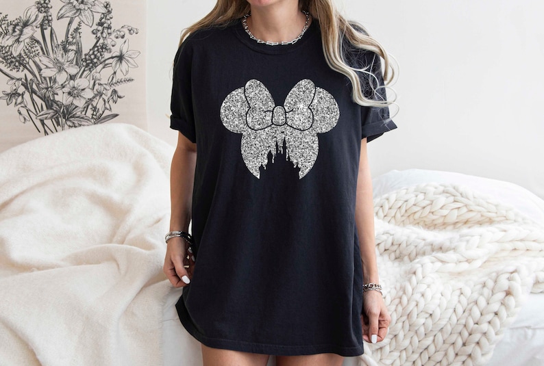 Puede incluir: Camiseta negra con un lazo de purpurina plateada y un dise&ntilde;o de castillo.