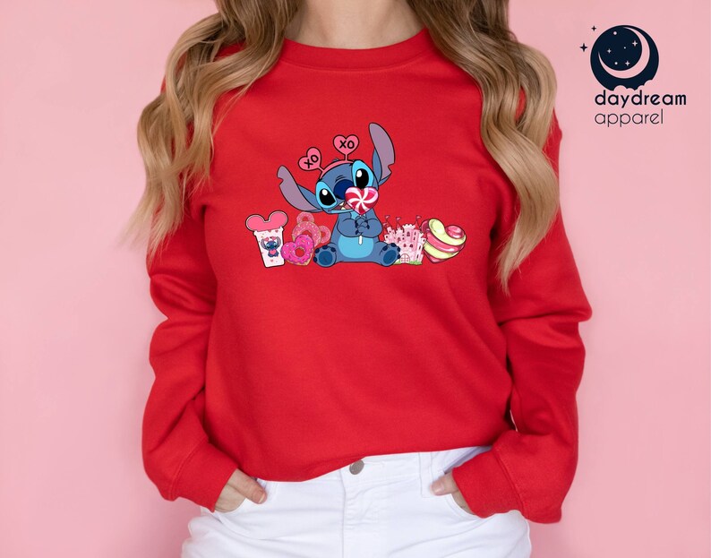 K&ouml;nnte beinhalten: Roter Pullover mit einer blauen Stitch-Figur, die einen Lolli h&auml;lt und von Herzen und S&uuml;&szlig;igkeiten umgeben ist. Der Text "XO" befindet sich auf einem Herz &uuml;ber Stitch's Kopf.