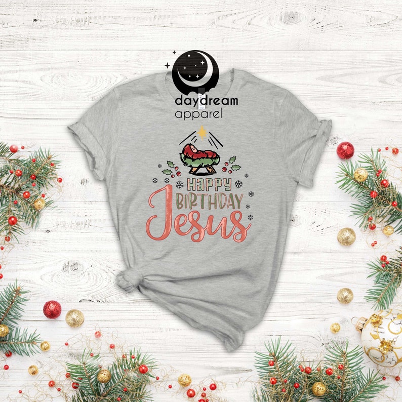 May include: A gray t-shirt with a Christmas nativity scene and the text "Happy Birthday Jesus" in pink and gold lettering.