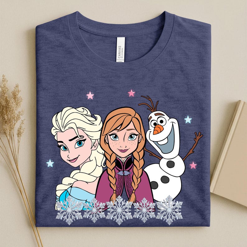 May include: Navy blue t-shirt featuring Elsa, Anna, and Olaf from Frozen. The graphic includes snowflakes and stars. The shirt is made of a soft material and is suitable for casual wear.