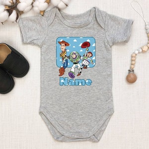 May include: Gray baby onesie with a blue and white cartoon image of Woody, Buzz Lightyear, and Jessie from Toy Story. The text "Name" is printed below the image.