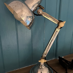 May include: A chrome desk lamp with a flexible arm and a white knob. The lamp has a white shade and a white bulb.