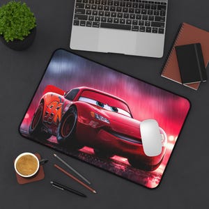 Puede incluir: Una alfombrilla de escritorio rectangular que muestra un coche de carreras rojo brillante con el número 95 impreso en el lateral. El coche tiene grandes ojos azules en el parabrisas y se sitúa sobre un fondo oscuro y lluvioso con luces rojas.
