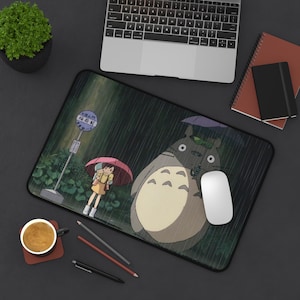 Pode incluir: Um tapete de rato retangular com uma cena de O Meu Vizinho Totoro, apresentando um grande Totoro cinzento com um guarda-chuva roxo e uma pessoa com um guarda-chuva vermelho numa paragem de autocarro à chuva. Tem uma borda preta.