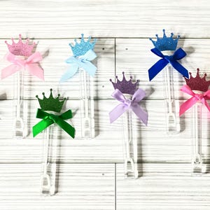 May include: A set of eight clear plastic wands with glitter crowns and bows. The crowns are in various colors, including silver, pink, blue, green, purple, and gold. The bows are in matching colors.