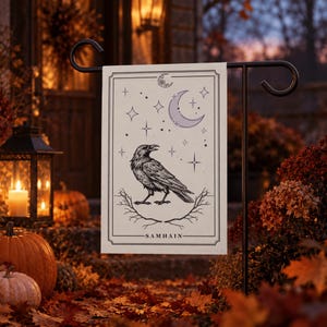 Op de afbeelding: Een rechthoekige tuin vlag met een zwart-witte illustratie van een raaf die op kale takken zit. Boven de vogel staan sterren en een maansikkel. Het woord SAMHAIN staat onderaan in een zwart kader gedrukt.