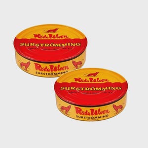 May include: Two round, yellow and red cans of Surströmming, a Swedish fermented herring. The cans have a red band around the middle with the word "SURSTRÖMMING" in white. The top and bottom of the cans are yellow with the words "Röda Ulven" and a wolf illustration.